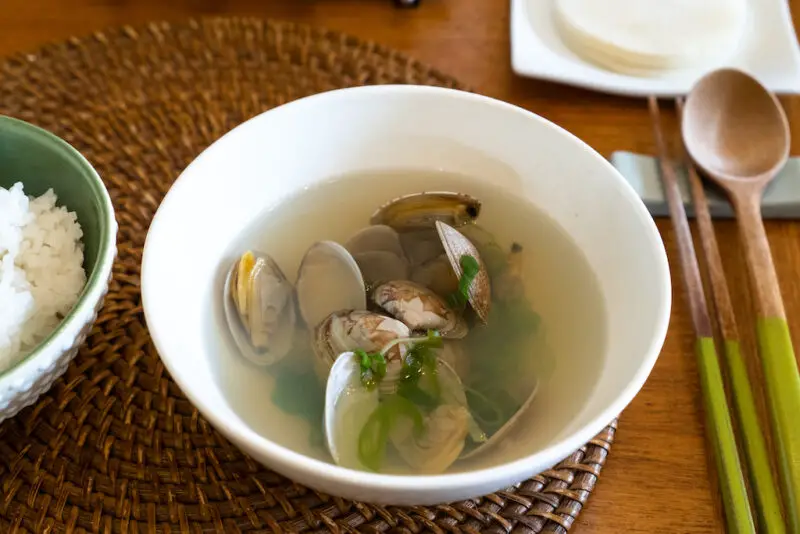 An overhead shot of jogaetang on a table mat next to a wooden set of chopsticks and spoon.