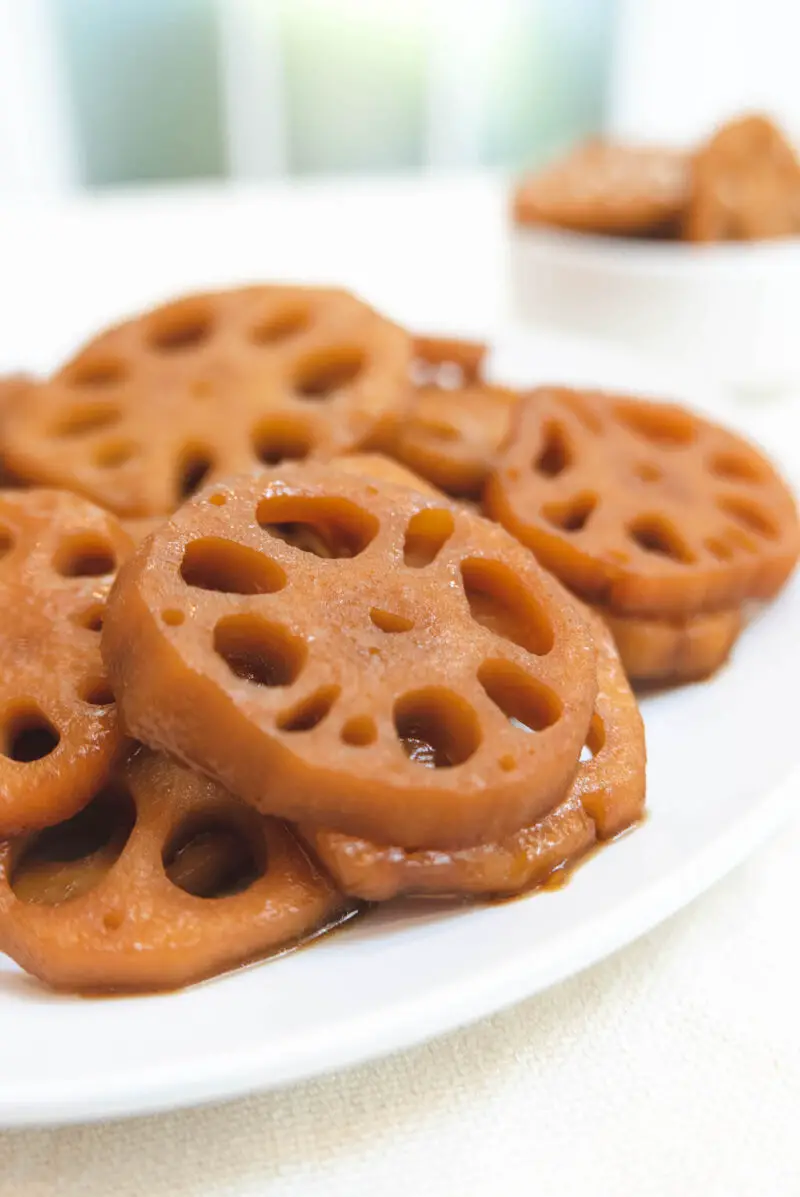 A side shot of Korean braised lotus roots on a white plate. The lotus roots are now brown from being raised in a soy sauced based sauce. 