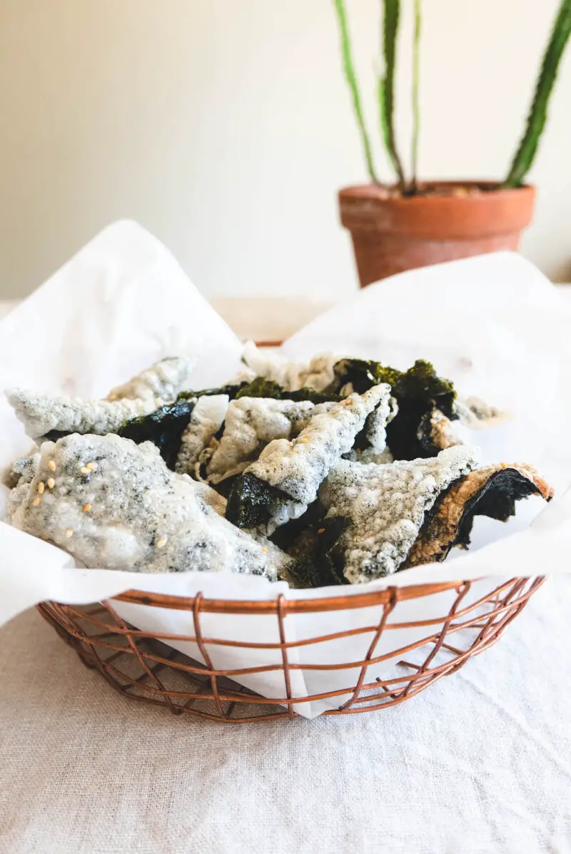 A side shot of this Korean rice paper fried seaweed snack in metal basket. The snack sits in parchment in the basket.