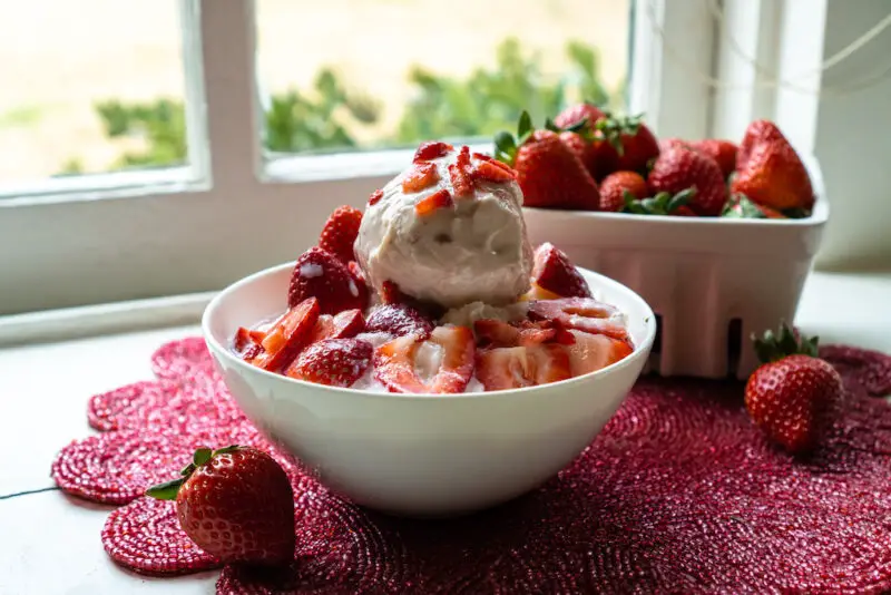 Korean shaved ice topped with strawberries and ice cream. Strawberries sit in the background. 