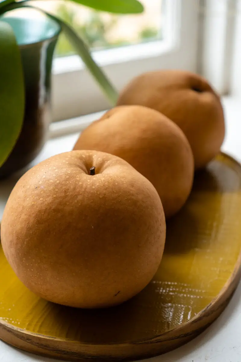 Three round Korean pears lined up on a yellow tray.