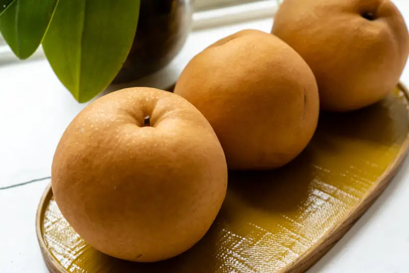 Three Asian pears lined up on an oval yellow tray. 