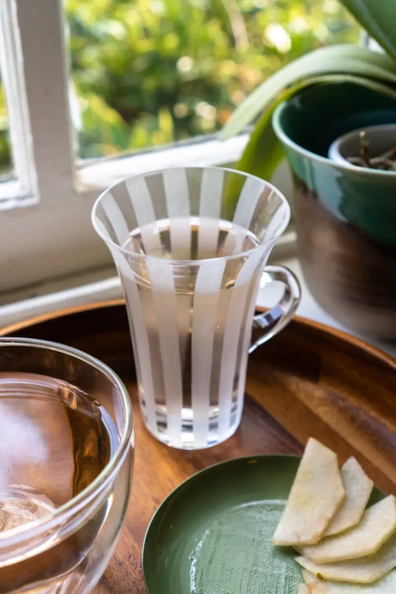 A side shot of a glass of tea in a striped glass mug. It sitts next to another glass of omija tea and pears. 