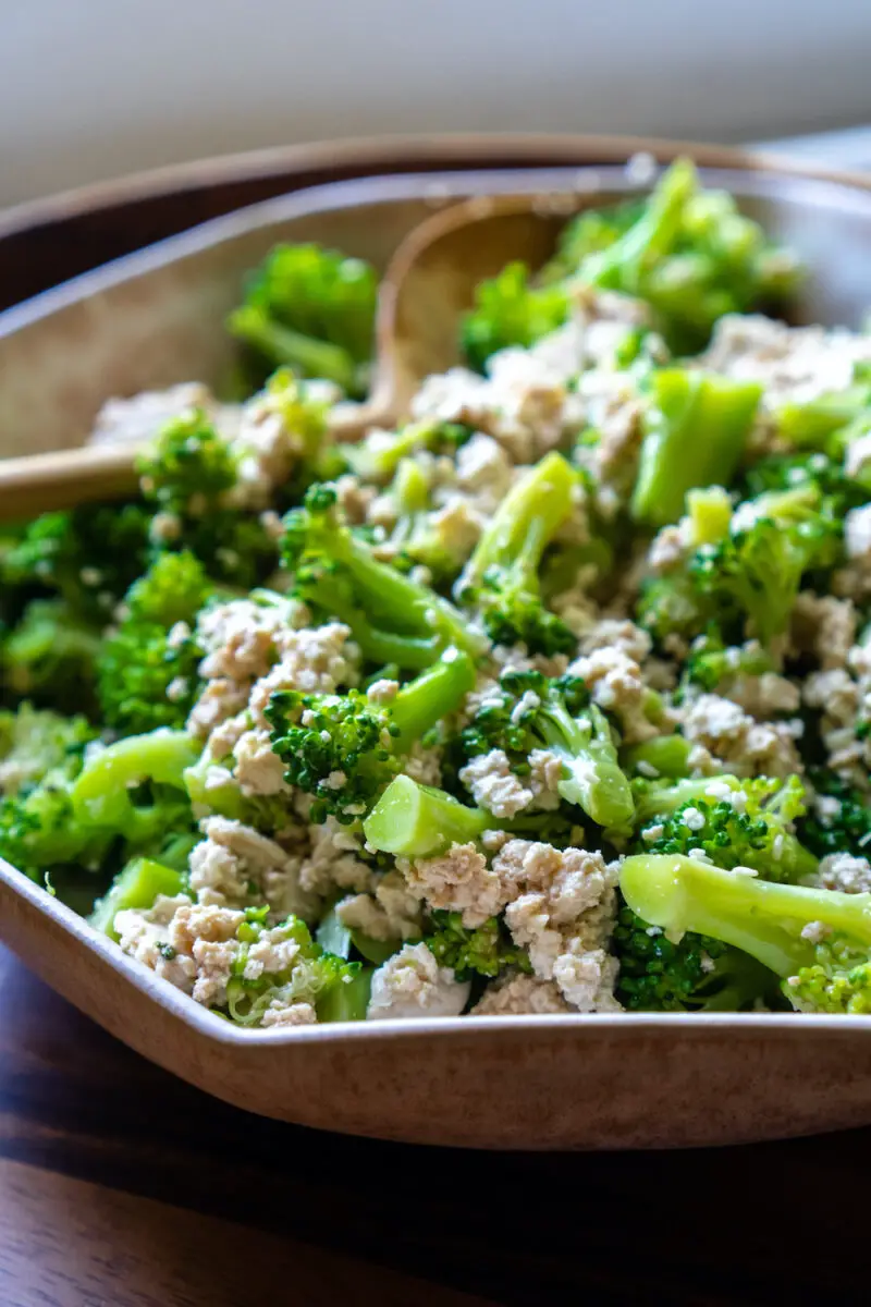 A closeup side shot of Korean broccoli tofu muchim. The dish sits in a bowl with a wooden spoon.