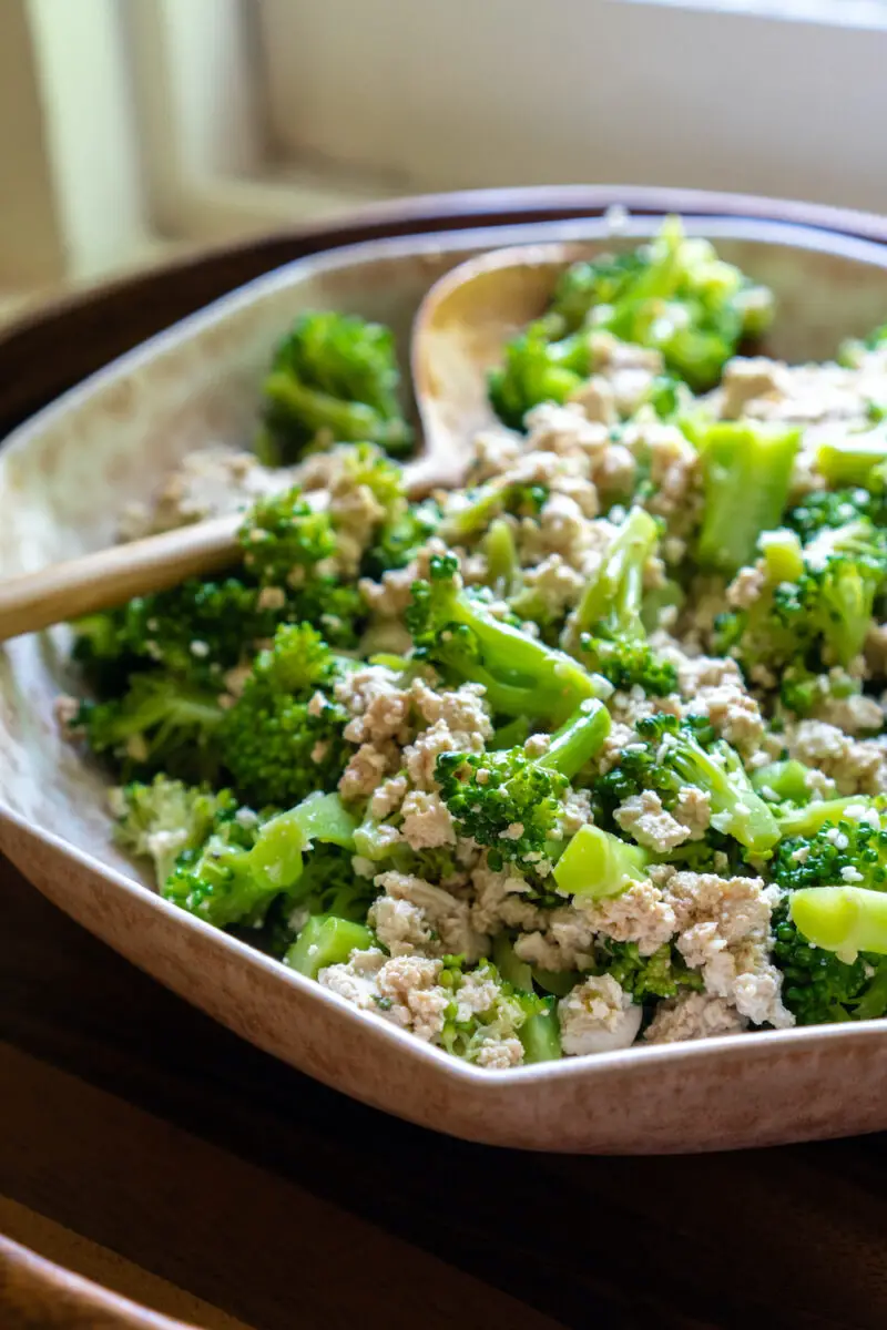 A closeup side shot of Korean broccoli tofu side dish in a bowl. A wooden spoon sits next to the dish. 