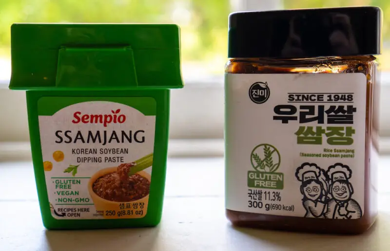 Two containers of gluten-free ssamjang on a window sill. One container is green. One container is clear where you can see the ingredients.