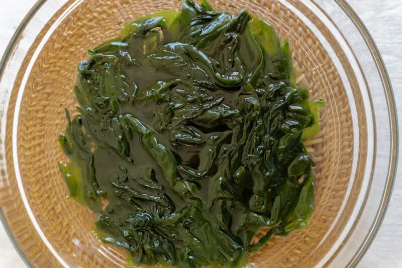 An overhead shot of miyeok soaking in water in a clear bowl. The bowl sits on a brown mat.