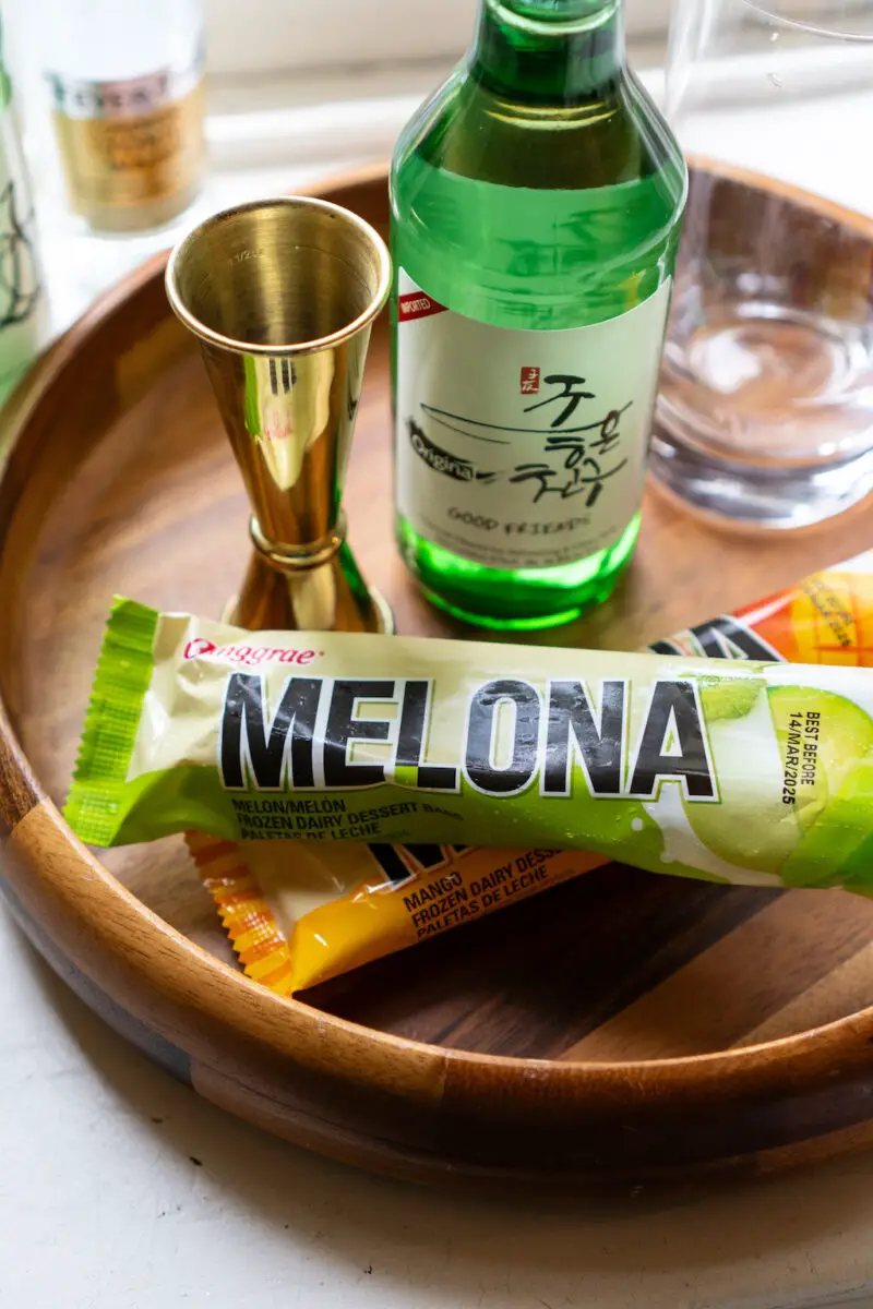 A photo of Korean Melona ice cream bars on a wooden tray. Soju and a jigger sit next to the ice cream. 