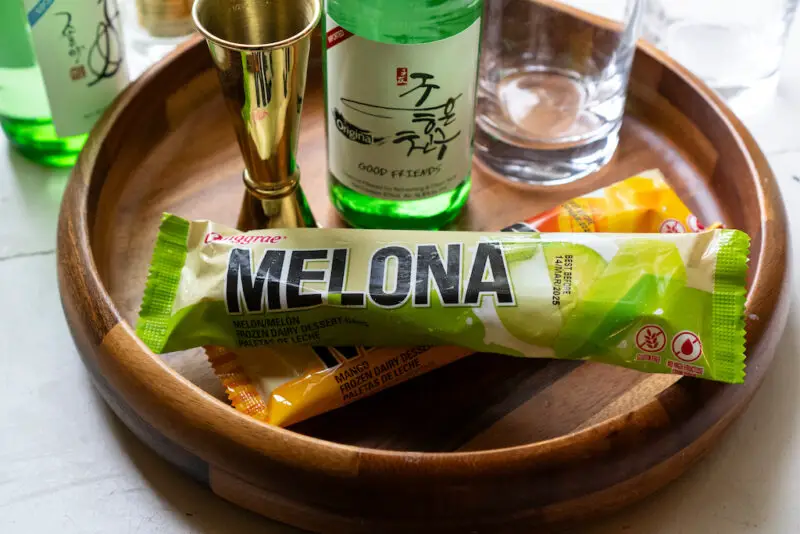 A photo of Korean Melona ice cream bars on a wooden tray. Soju and a jigger sit next to the ice cream. 