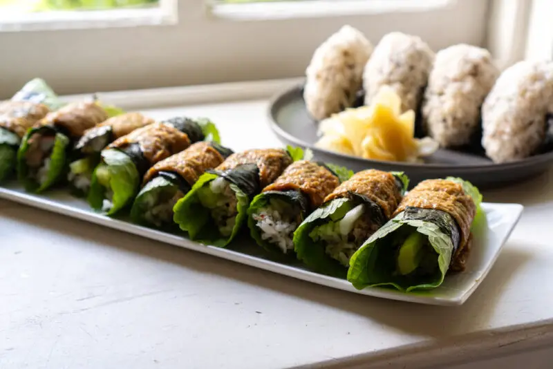 A shot Korean-style inari sushi next to rice balls and ginger on a window sill. 