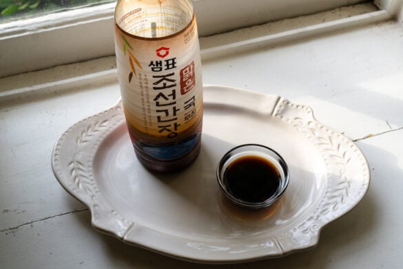 An overhead shot of Korean soup soy sauce in a small bowl next to the brand container.