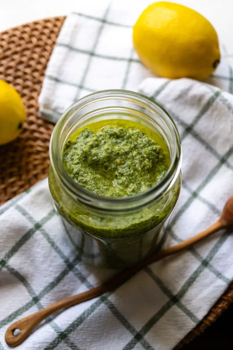 A side shot of perilla pesto in a glass jar. The jar sits next to a wooden spoon and a cloth napkin. 