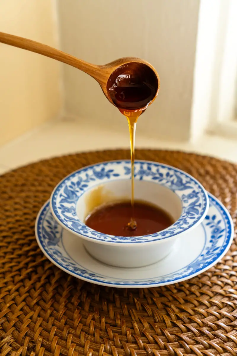 Kkul in a blue and white bowl on a wicker mat. Kkul is being poured from a wooden spoon into the bowl. 