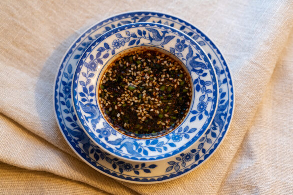 An overhead photo of Korean pancake sauce in a blue and white small bowl. The bowl sits on a matching plate. Both sit on a cream table cloth.