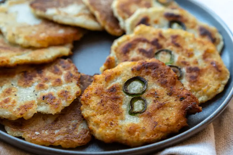 Korean potato pancake on a plate. The round potato fritters have green hot peppers in the center. 