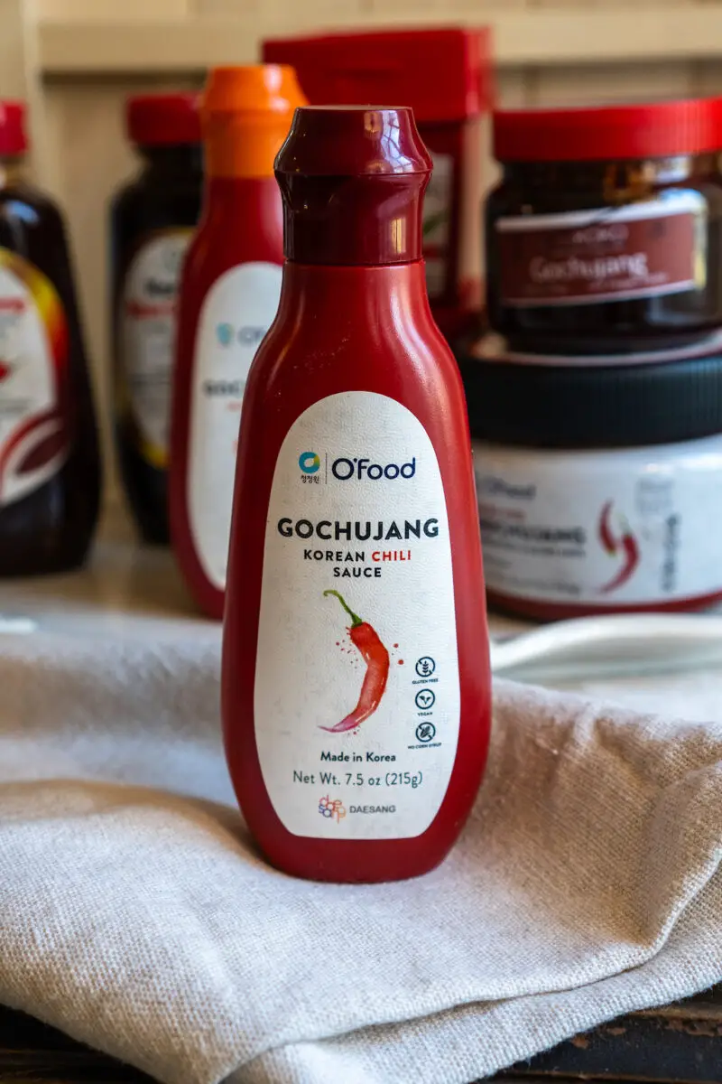 A closeup shot of Korean chili sauce on a cream table cloth. Other containers sit in the background. 
