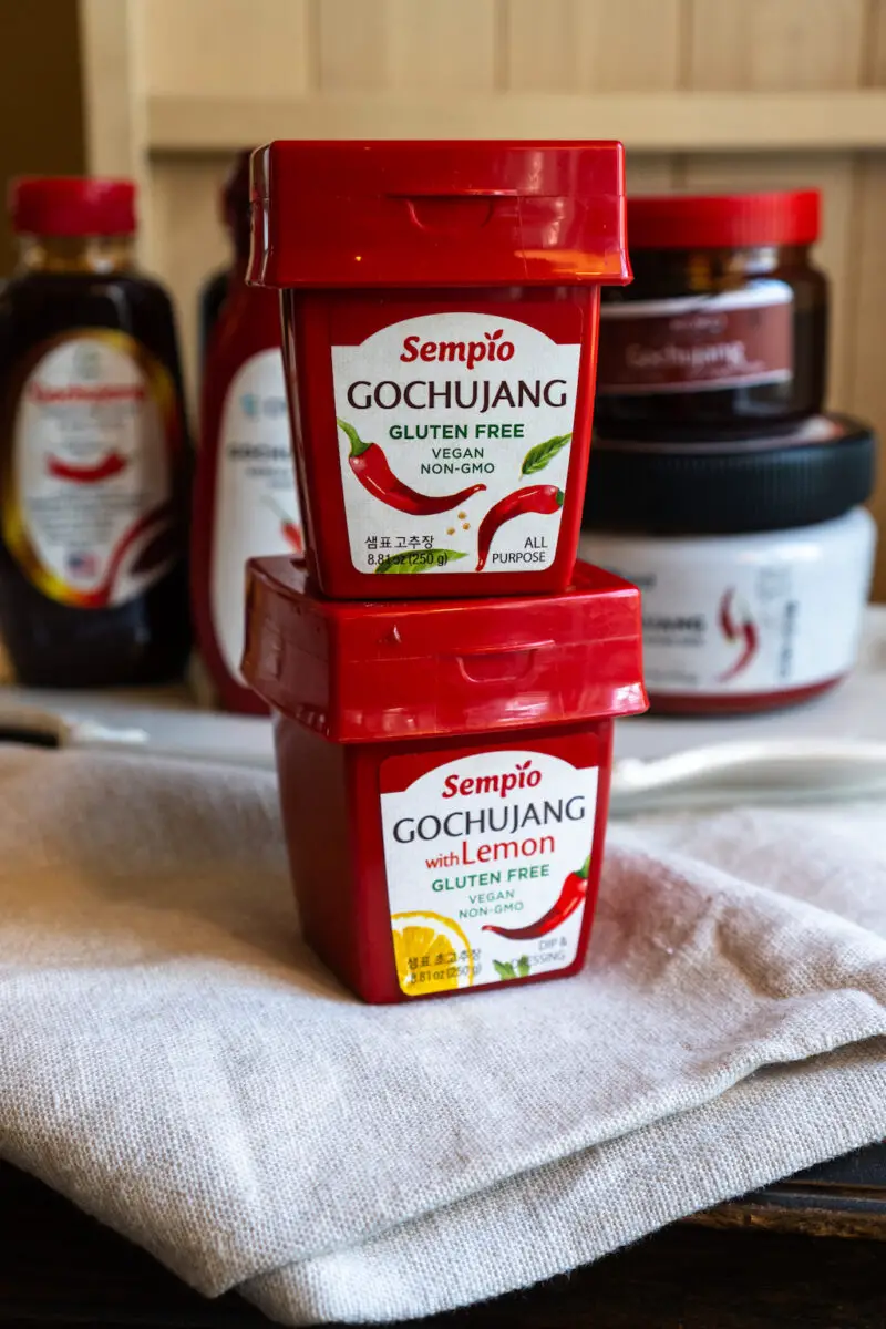 Sempio gluten-free gochujang containers sitting on a cream table cloth. Other containers sit in the background. 