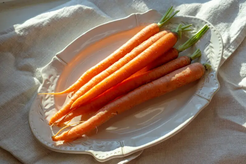 An overhead shot of a pile of carrots on a cream oval tray.