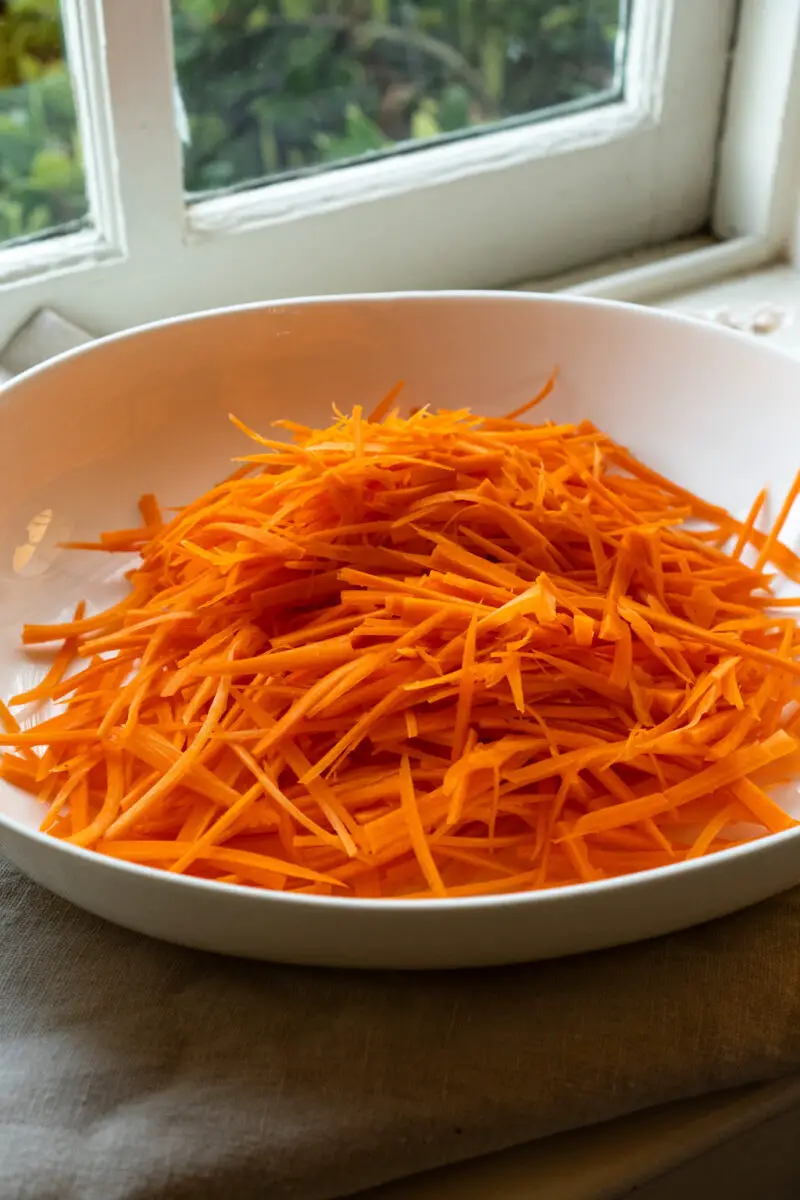 A side shot of a bowl of julienned carrots in a white bowl. 