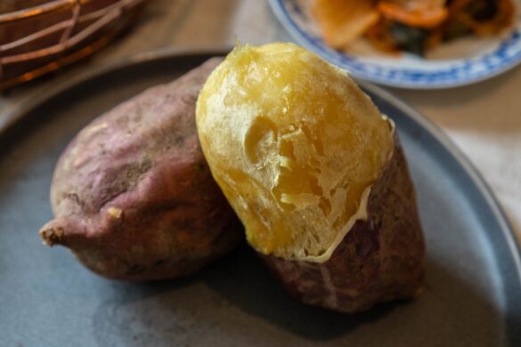 An overhead photo of baked Korean sweet potato on a grey plate. It sits next to kimchi.
