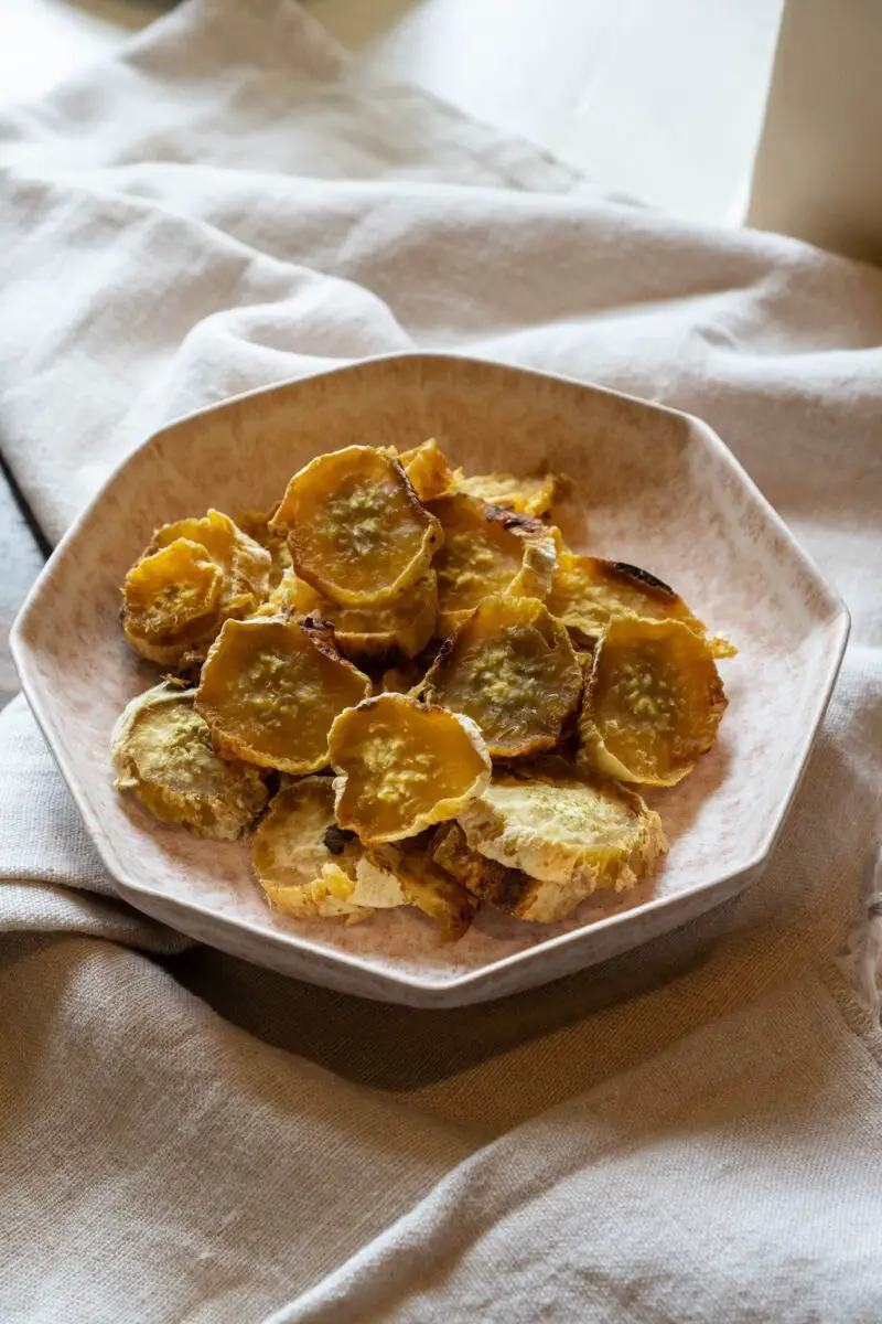 Korean dried sweet potato snack in a pink bowl on a table with a table cloth. The potatoes are in a pile. 