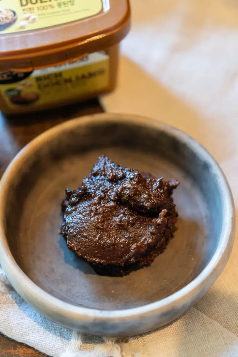 An overhead photo of a bowl of Korean soybean paste sitting next to the original container. 