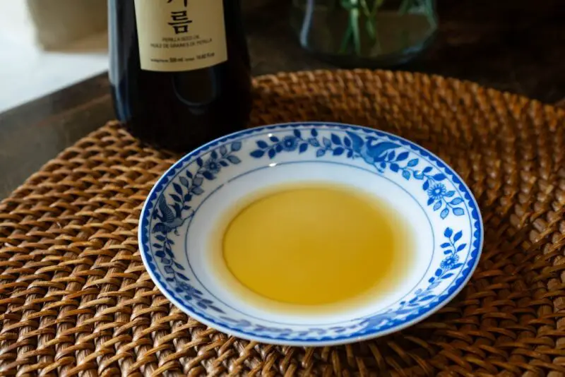 A photograph of deulgireum on a blue and white curved plate. The bottle sits in the background. It sits on  a wicker place mat. 