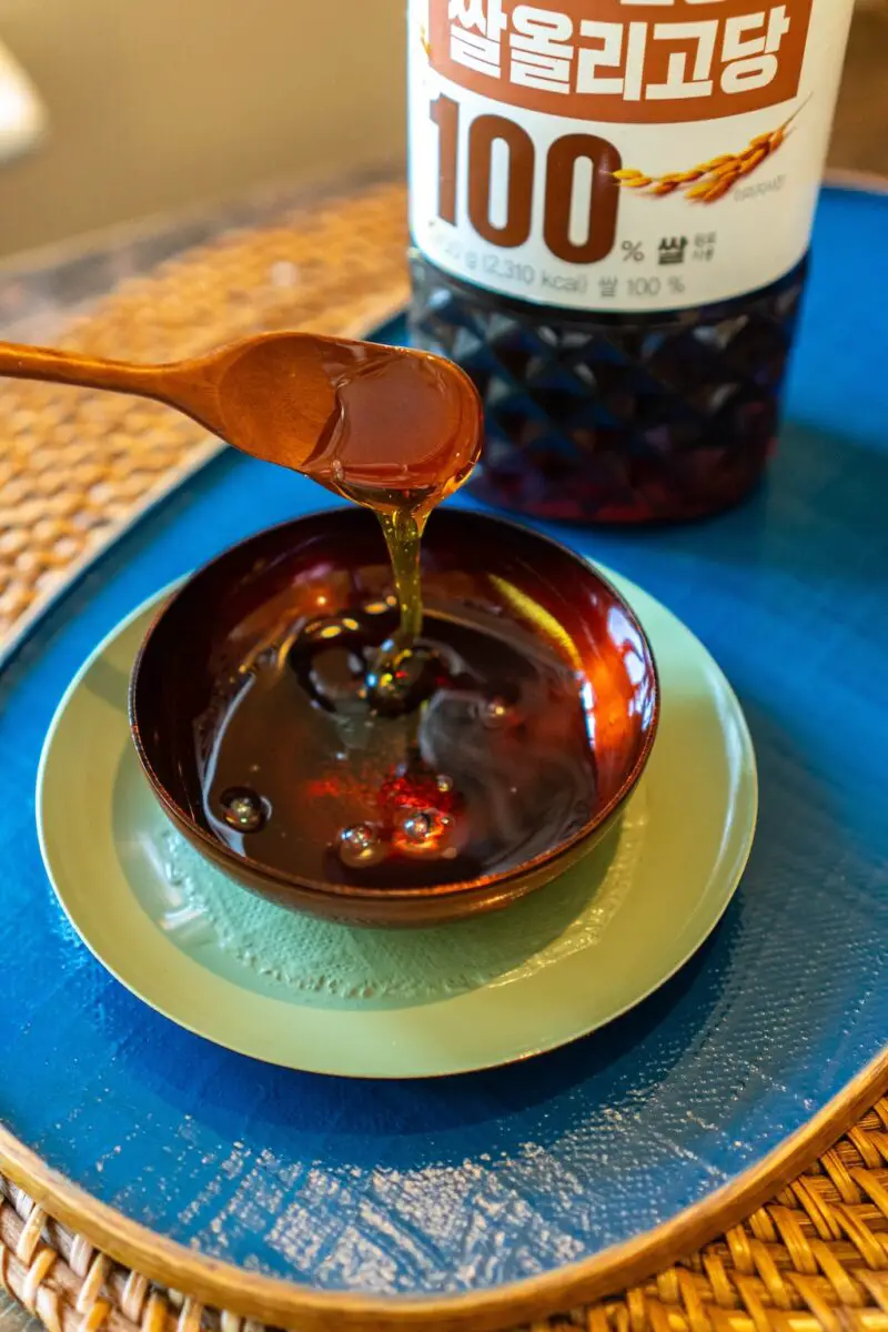 A photo of sweetener in a small bowl. The bowl sits on a green plate. The plate sits on a blue tray. A wooden spoon has been dipped into the bowl.