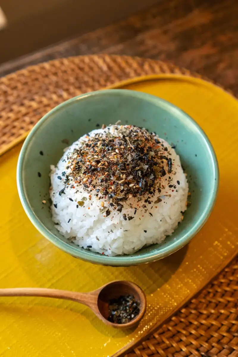 Perilla furikake over white rice in a bowl. The rice sits in a green bowl on a yellow tray. 