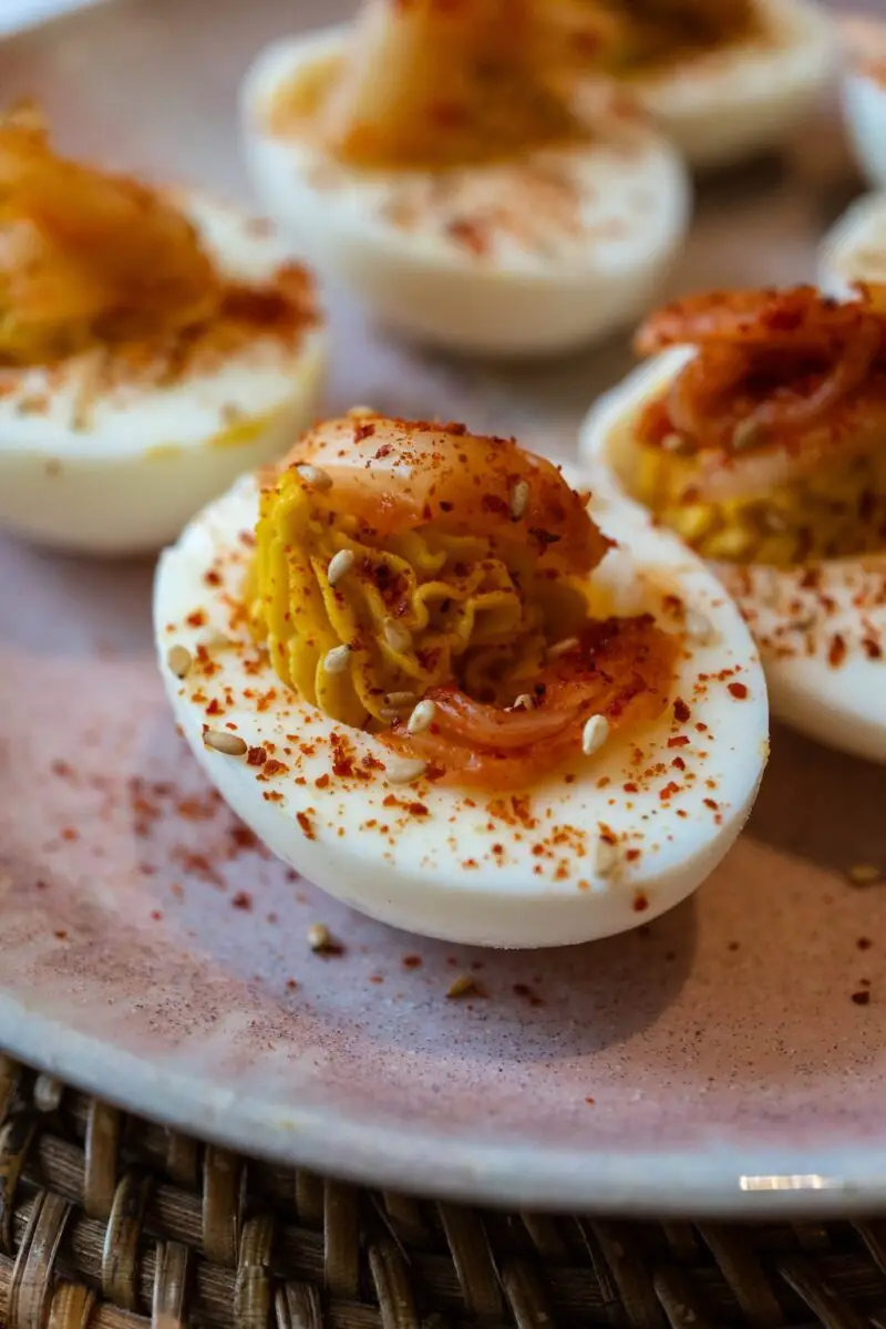 A photo of kimchi deviled eggs on a pink plate. The deviled eggs are topped with sesame seeds. 